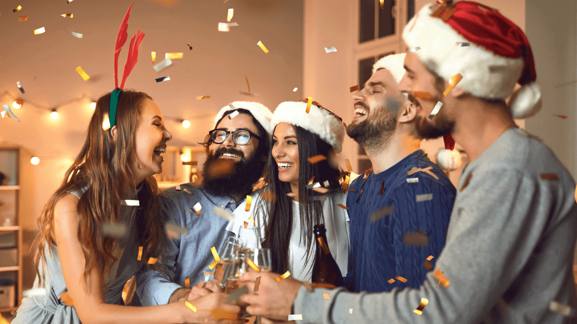 Cheerful Friends Clinking Glasses during Cozy Christmas or New Year Party at Home