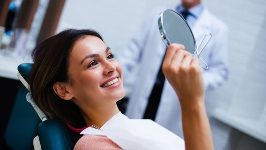 Smiling woman looking at mirror at endodontist office.