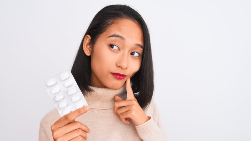 Young woman with confused look holding up antibiotics.