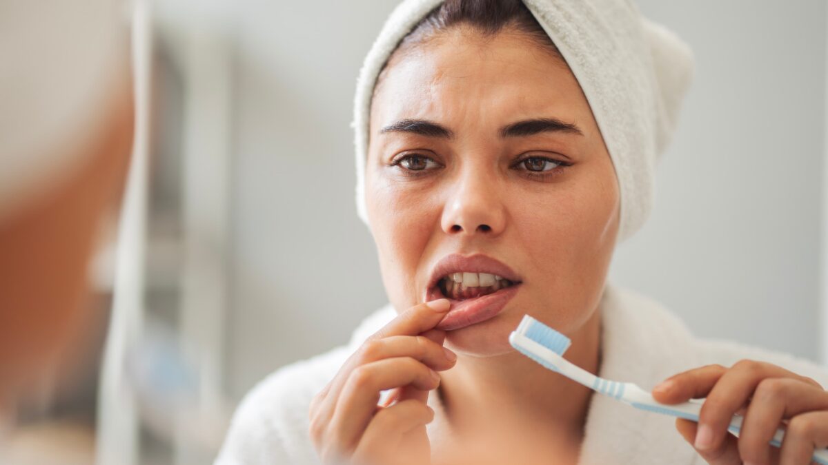 Woman brushing her teeth and looking at her gums.